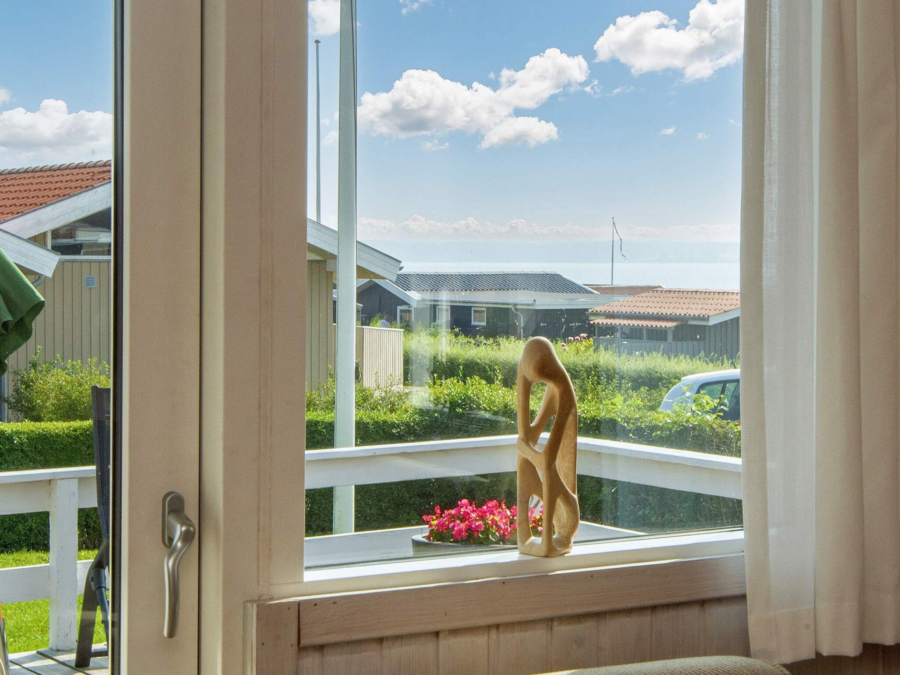 A window with a view of a residential area, a wooden sculpture, and a flower pot on the windowsill.