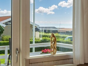A window with a view of a residential area, a wooden sculpture, and a flower pot on the windowsill. - 6 Person Holiday Home in Juelsminde (Horsens)