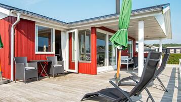 A red building with a covered patio area, outdoor seating, and a green umbrella.