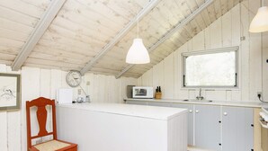 A kitchen with a wooden ceiling, white cabinets, a wooden chair, a microwave, and a window. - 4 Person Holiday Home in Oksbol (Oksbol)