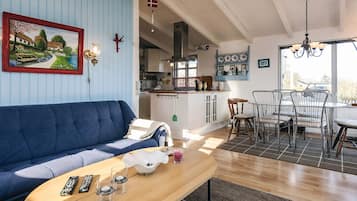 Una sala de estar con un sofá azul, una mesa de centro de madera y un comedor con sillas de metal.