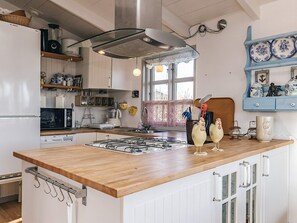 A kitchen with a wooden countertop, white cabinets, a Bosch refrigerator, a Bosch microwave, a gas stove, and decorative items.