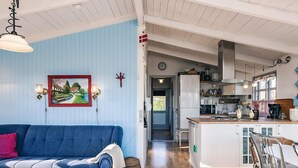 Uma sala de estar com um sofá azul, uma mesa de centro de madeira e uma área de cozinha com uma geladeira branca e armários de madeira.