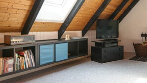 Une chambre à coucher aménagée dans un espace mansardé, avec un plafond en pente, une télévision, une bibliothèque et une cheminée.
