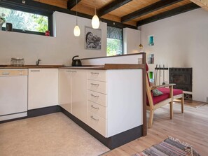 A modern kitchen with a built-in dishwasher, a wooden bench with a cushion, a fireplace, and pendant lighting.