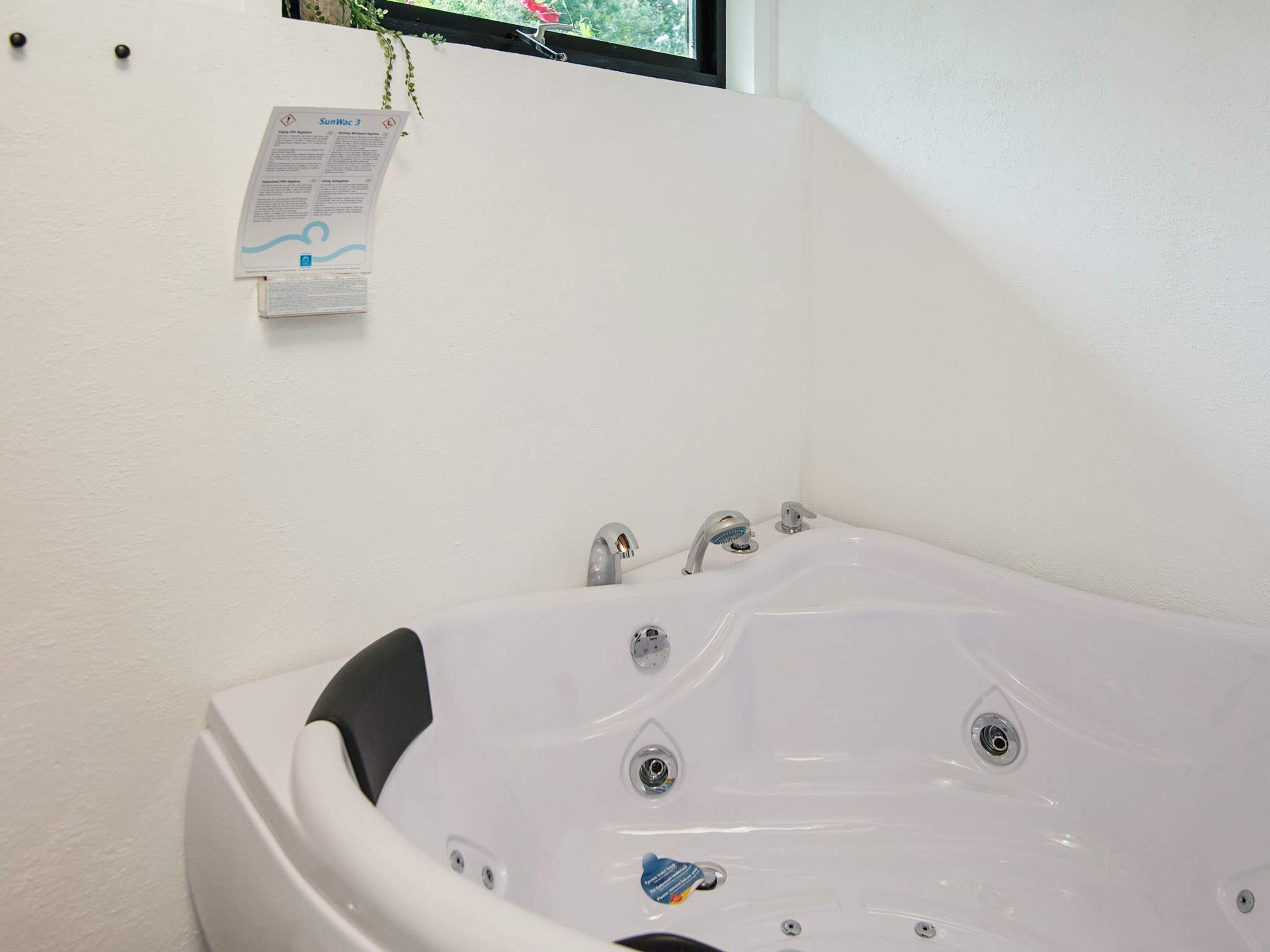 Une baignoire blanche dotée de plusieurs robinets et d’une pomme de douche, un petit flacon de shampoing et un panneau de sécurité fixé au mur.