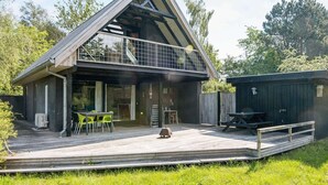 Une maison moderne dotée d’une terrasse en bois, d’un patio couvert et d’un petit espace de détente extérieur.