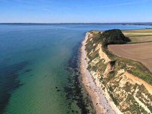 Luchtbeeld van een kustlandschap met een helder strand, een grasveld en een waterpartij.