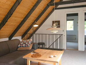 A loft bedroom with a sloped ceiling, a wooden table, a sofa, a small stool, and a picture frame on the wall.