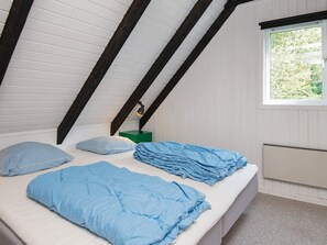 A bedroom with a sloped ceiling, a window with a view of greenery, a bedside table with a lamp, and a bed with blue bedding. - 4 Star Holiday Home in Knebel (Knebel)