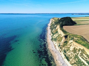 Luchtbeeld van een kustgebied met een strand, helder water en omliggende velden.
