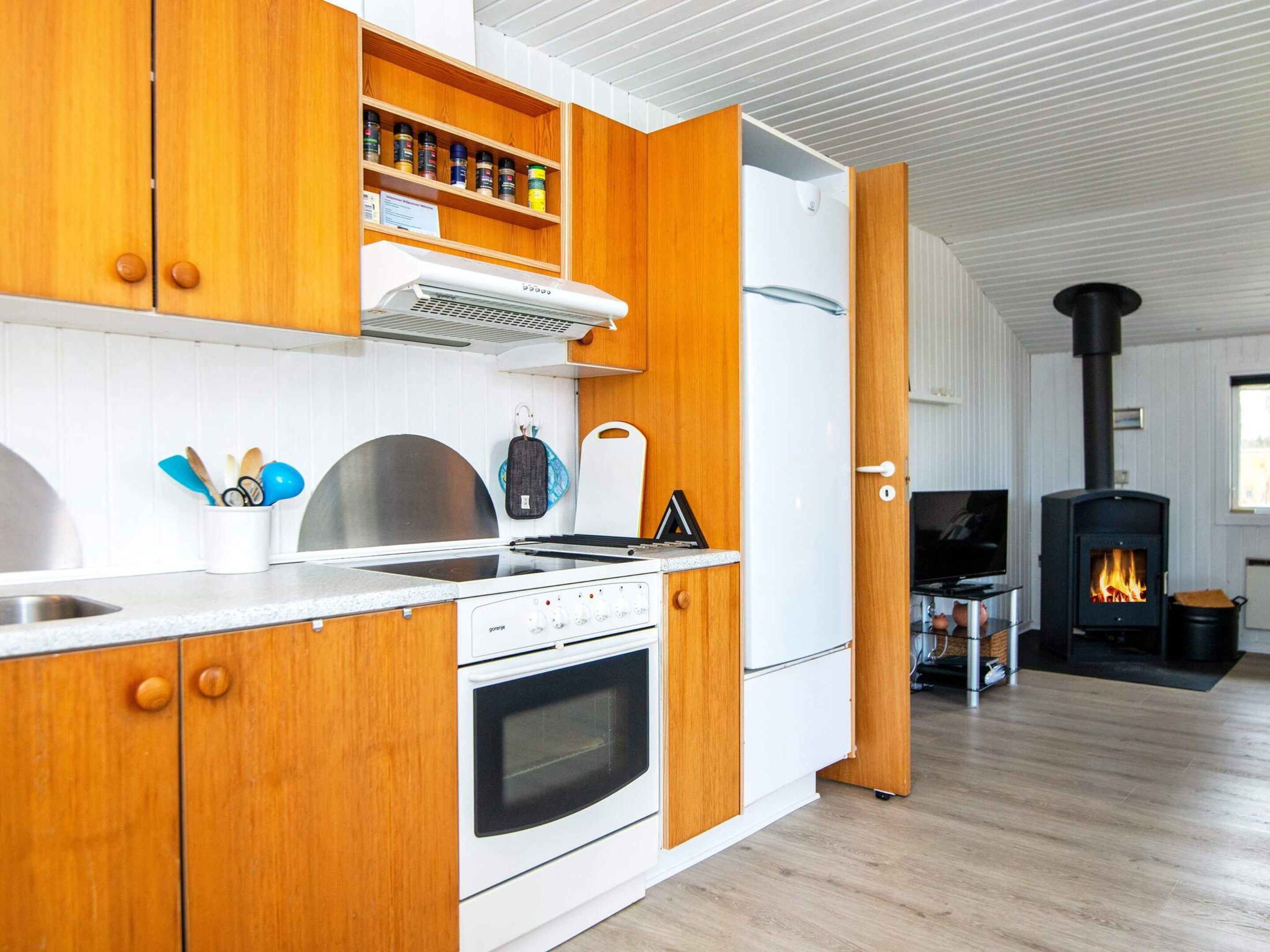 A modern kitchen with wooden cabinets, a built-in oven, a stovetop, and a wood-burning stove.