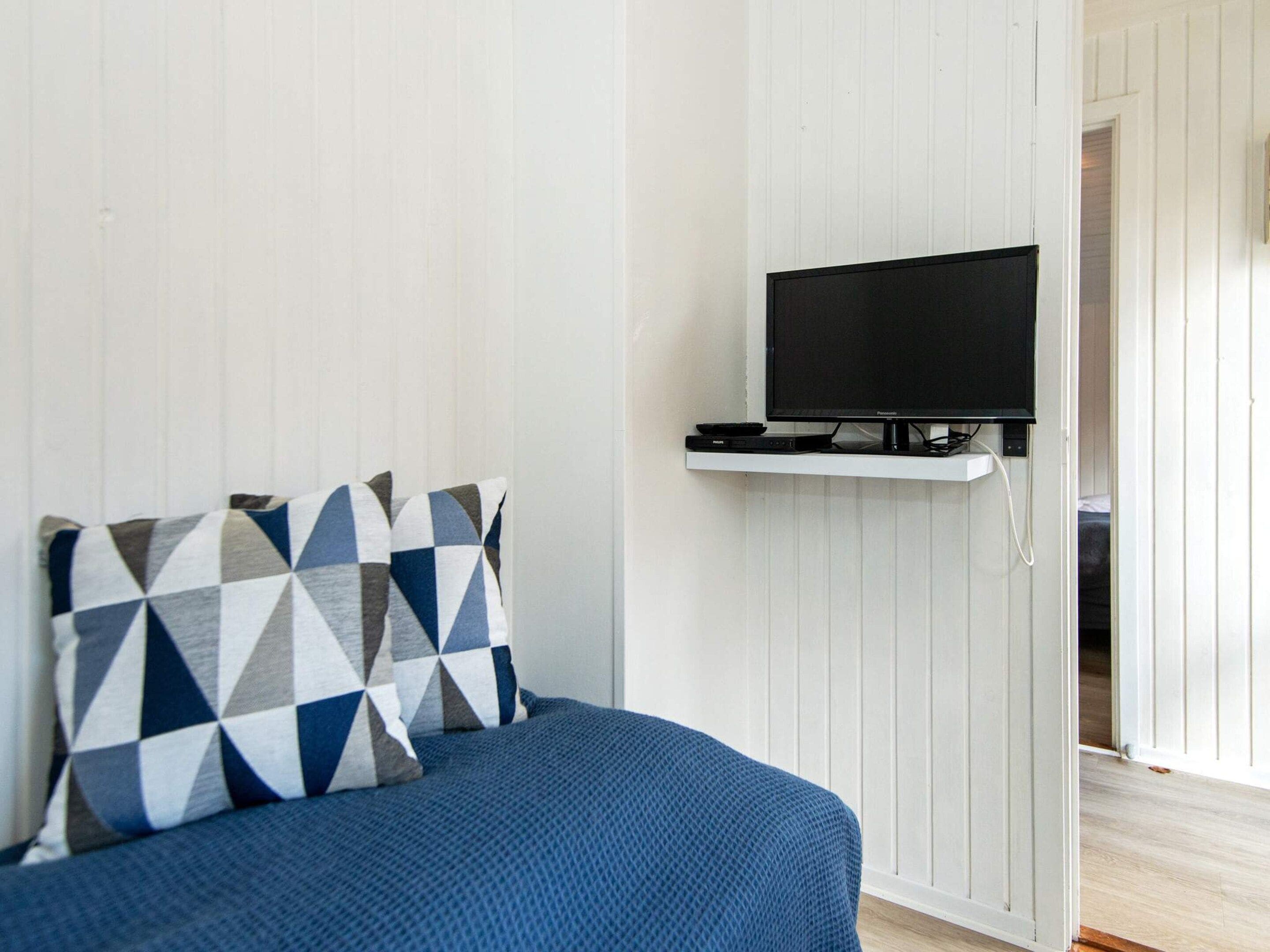 A room with a bed, a television mounted on a white wall, and a door leading to another room.