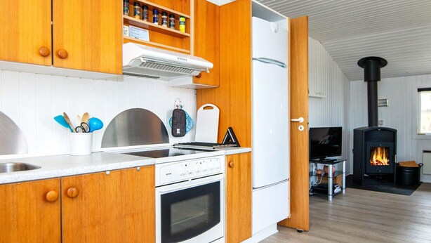 A modern kitchen with wooden cabinets, a built-in stove, and a wood-burning stove.