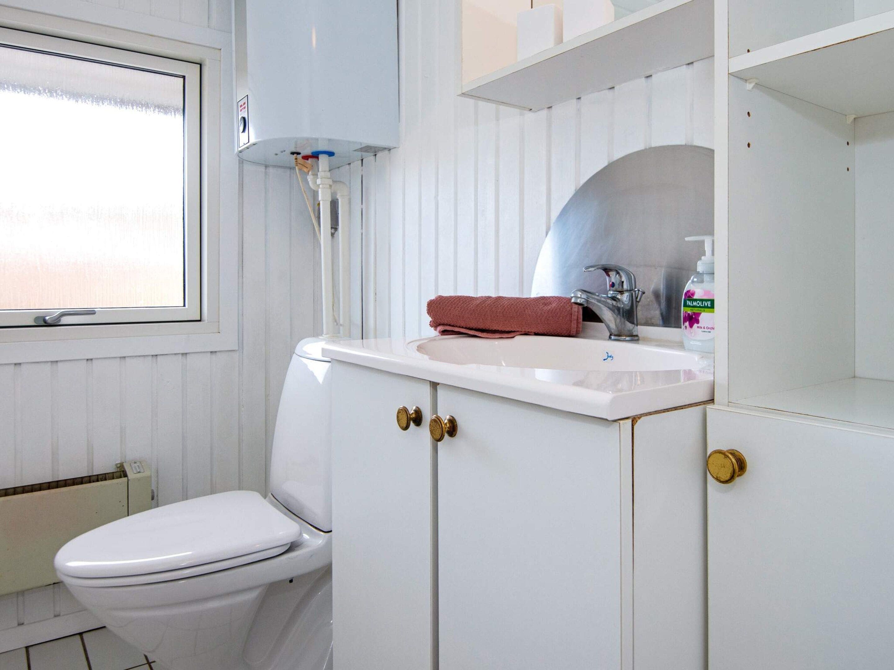 A bathroom with a toilet, sink, and window.