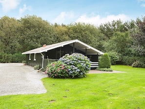 A small, single-story building with a sloped roof, a covered porch, and a gravel driveway.