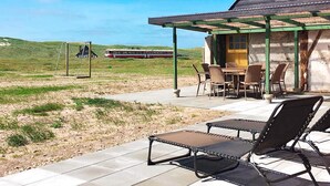 Een overdekt terras met buitenmeubilair, een schommel en een uitzicht op een trein in de verte.