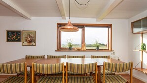 Een eethoek met een houten tafel en gestreepte stoelen, een hanglamp en een raam met uitzicht op de omgeving.