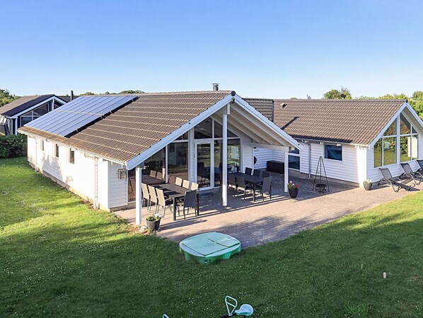 A two-story house with a patio area, a covered outdoor seating area, and a green lawn. - 5 Star Holiday Home in Stege (Stege)