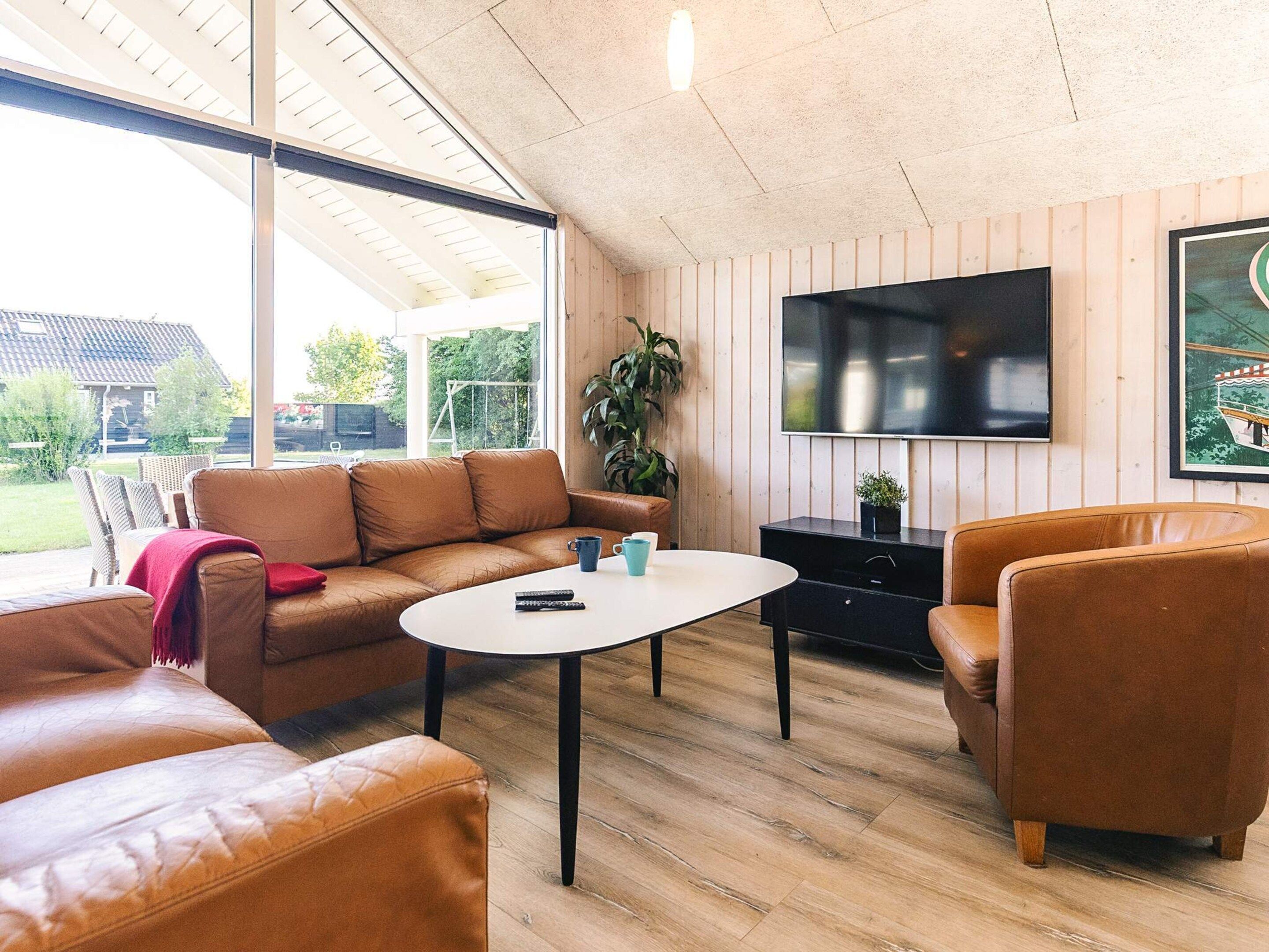 A modern living room with leather sofas, a coffee table, and a flat-screen TV mounted on a wooden wall.