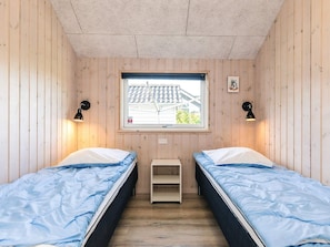 Quarto com duas camas, uma janela e um pequeno prateleira.
