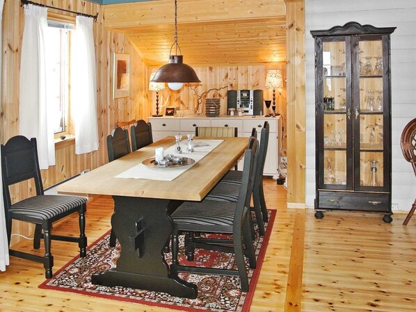 Ein Esszimmer aus Holz mit einem langen Tisch, Stühlen, einer Chandelieber und einem Schrank mit Glastüren.