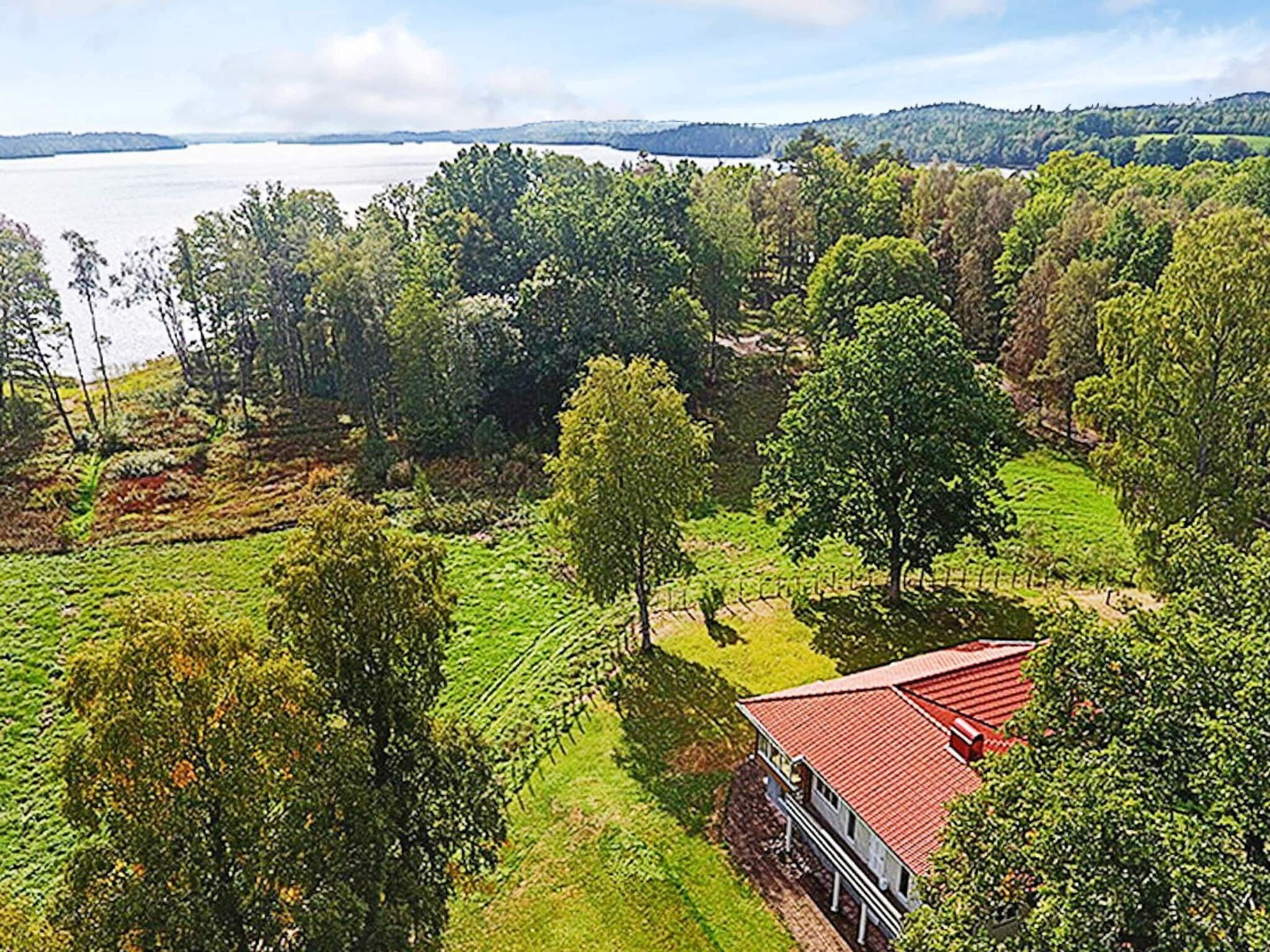 A house with a red roof surrounded by lush greenery and a lake in the background.