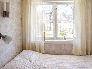 A bedroom with a bed, a window with sheer curtains, and a wall-mounted light fixture. - Holiday Home in Kalv (Kalv)