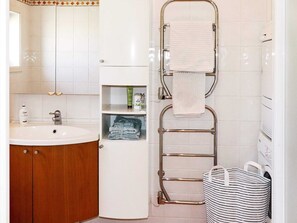 A bathroom with a wooden vanity, a sink, a mirror, a towel rack, and a storage cabinet. - Holiday Home in Kalv (Kalv)