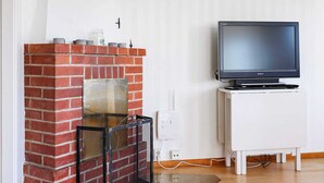 A living room with a brick fireplace, a white cabinet, and a television on a stand. - Holiday Home in Kalv (Kalv)