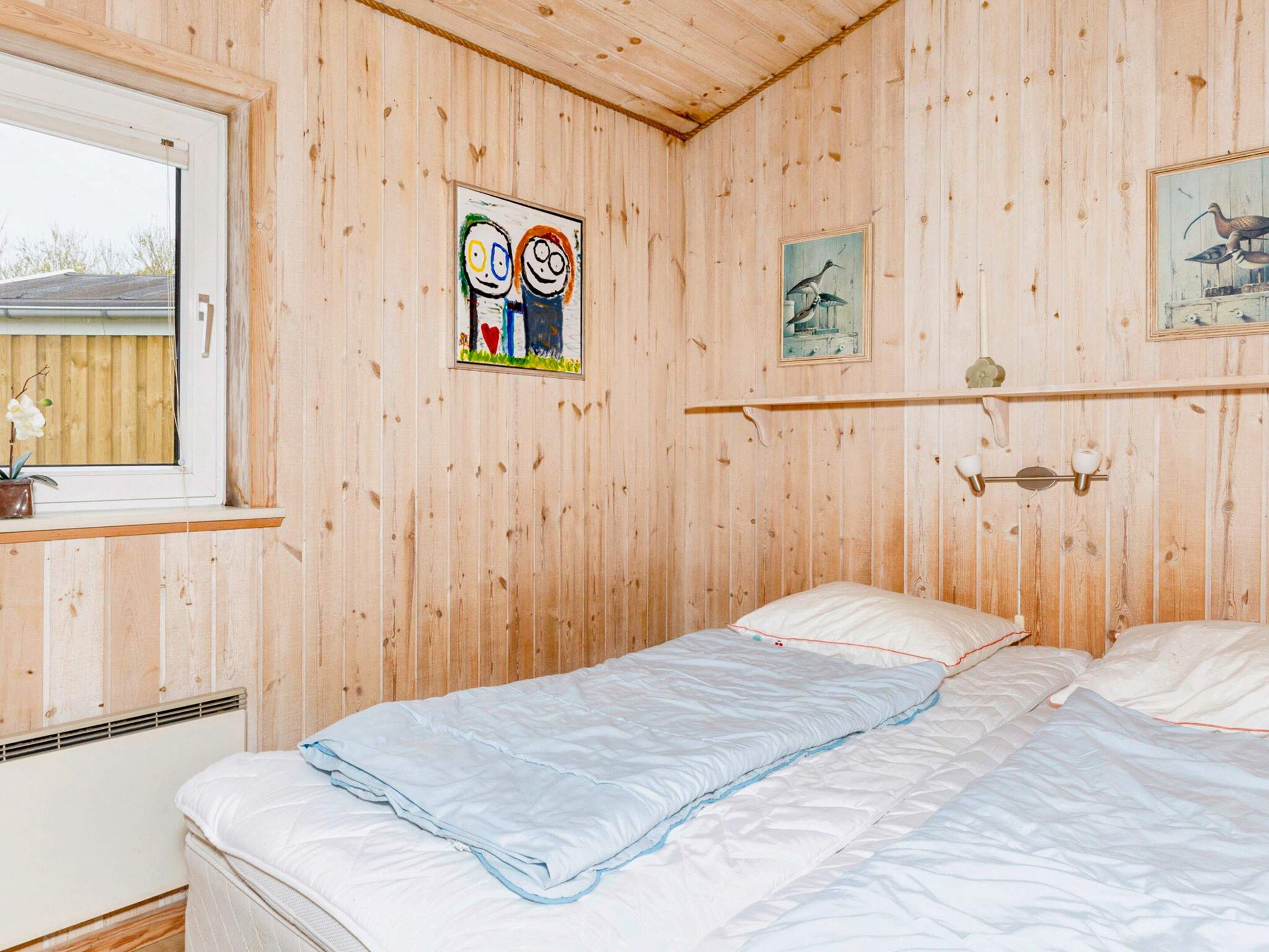 Ett rum med träpanel på väggarna, en säng med vita sängkläder, ett fönster med utsikt och konst på väggen.