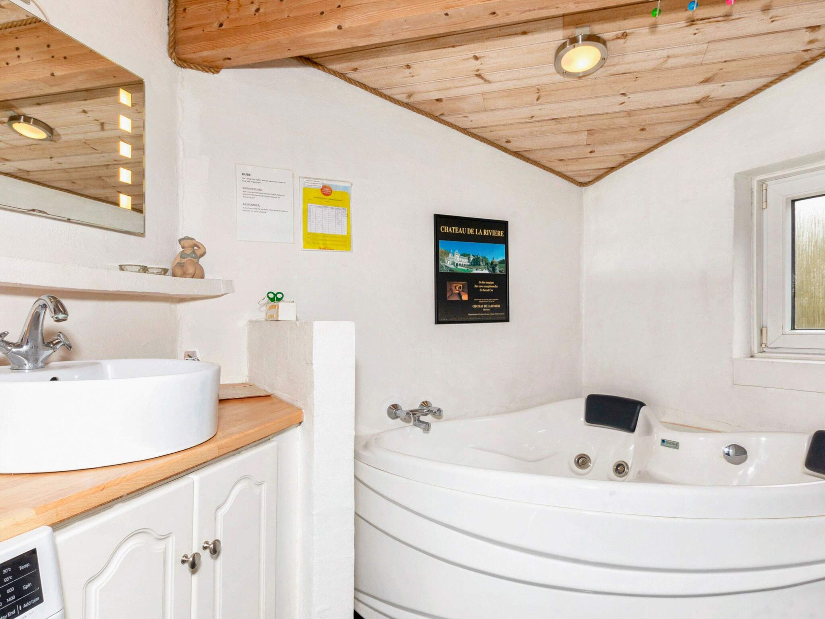 A bathroom with a white sink, a wooden countertop, a bathtub, and a mirror above the sink.