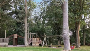 A playground with wooden structures and swings surrounded by trees.