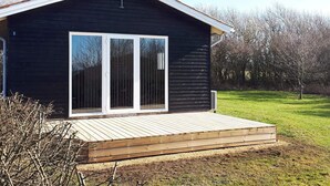 Une petite cabane en bois sombre, dotée d’une grande porte-fenêtre coulissante, d’une terrasse en bois et d’une cheminée.
