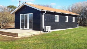 Une petite maison de plain-pied, à l’extérieur sombre, dotée d’une terrasse en bois et d’un toit en métal.