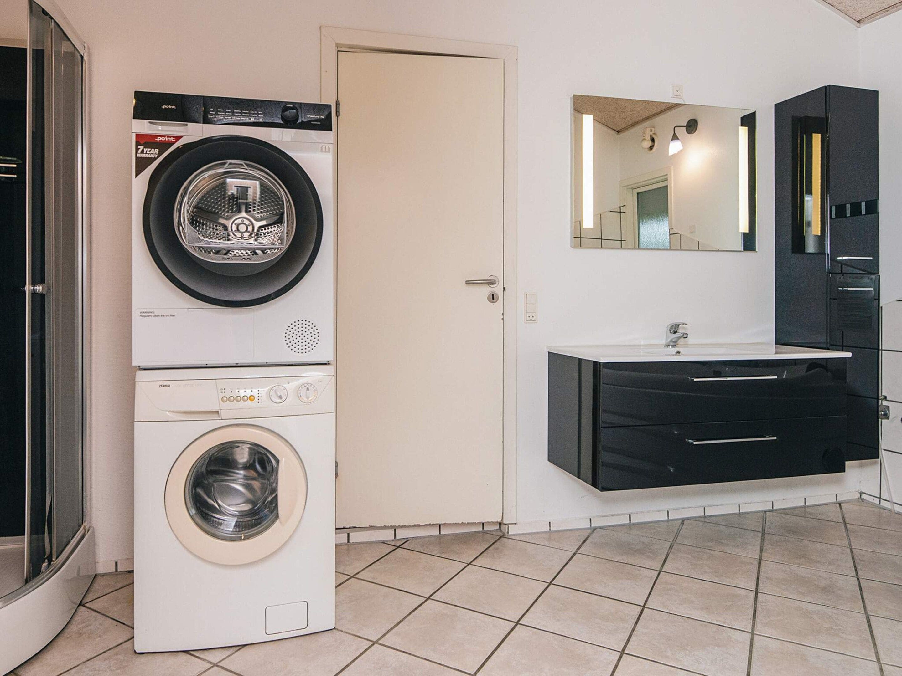 Une buanderie équipée d’un lave-linge et d’un sèche-linge à chargement frontal, d’un évier avec un miroir au-dessus, et d’une porte donnant sur une autre pièce.