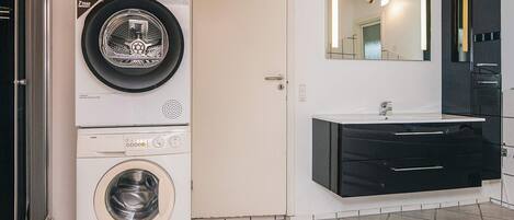A laundry room with a front-loading washer and dryer, a sink with a mirror above it, and a door leading to another room.