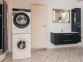 Un lavadero con lavadora y secadora de carga frontal, un lavamanos con espejo y una puerta que da a otra habitación.