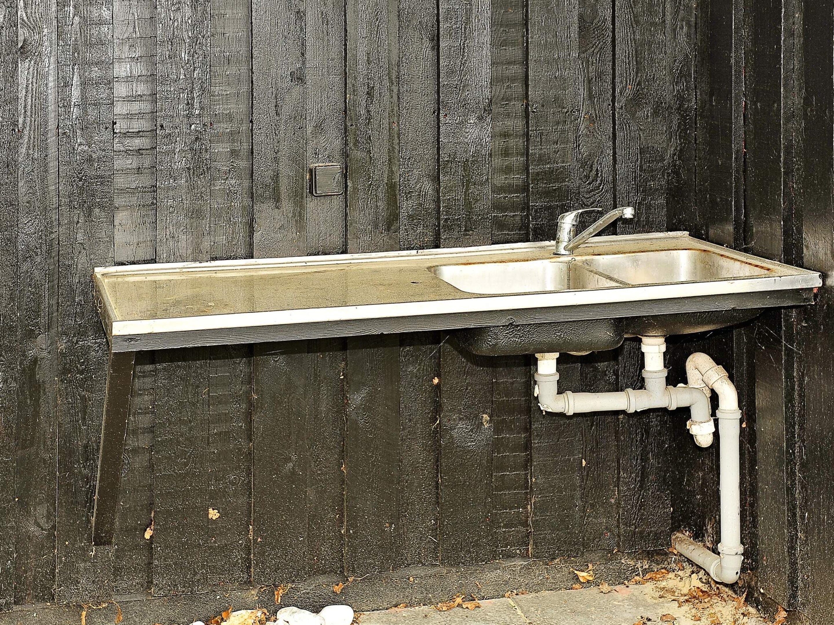 Ein Metallwaschbecken mit Wasserhahn, an einer Holzwand montiert, mit sichtbaren Rohren darunter.