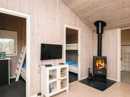 Una habitación con televisión, literas, un armario blanco y una estufa de leña.