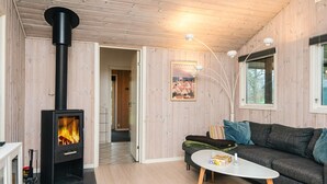 A cozy living room with a wood-burning stove, a sofa, a coffee table, and a poster on the wall. - Rustic Holiday Home in Ansager near Water (Ansager)