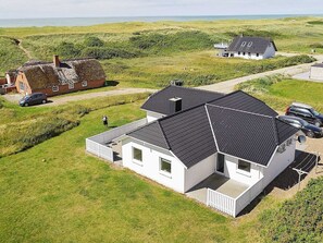 A white house with a dark roof, surrounded by green fields and a body of water in the background. - 5 Star Holiday Home in Harboore (Harboore)