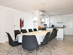 Une cuisine moderne avec des meubles blancs, une table à manger avec des chaises et un petit îlot central équipé d’appareils électroménagers.
