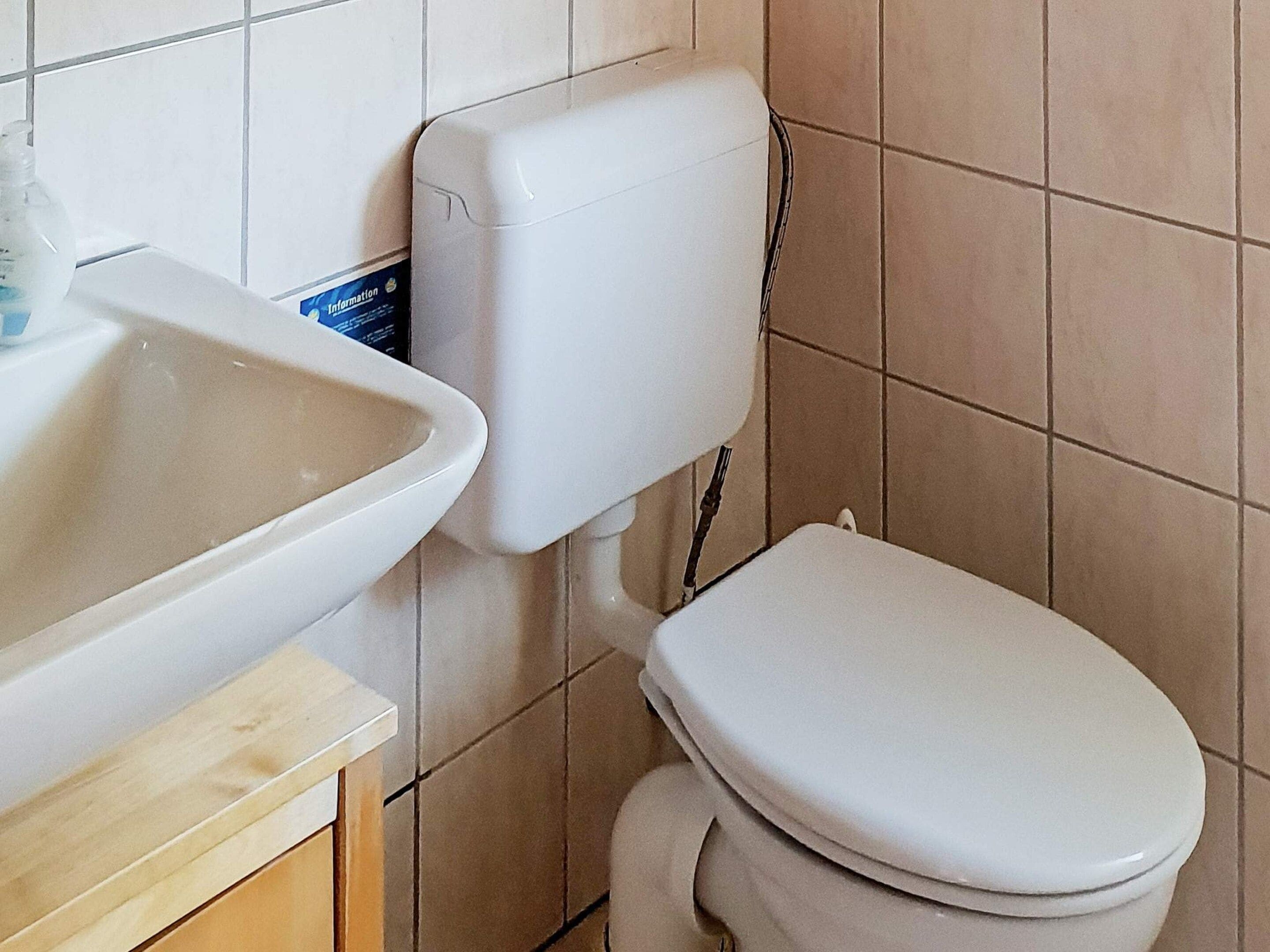Casa de banho com sanita branca, lavatório e painel informativo fixado na parede.