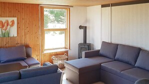 Een moderne woonkamer met een hoekbank, een klein tafeltje, een rieten mand en een houtkachel.