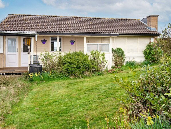 A single-story house with a tiled roof, a front porch, and a small garden with various plants and flowers.