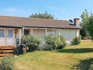 A single-story house with a tiled roof, a front porch with a bench, and a small garden area.
