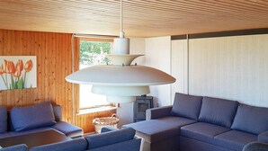 Een moderne woonkamer met een hoekbank, een houten plafond en een grote hanglamp.