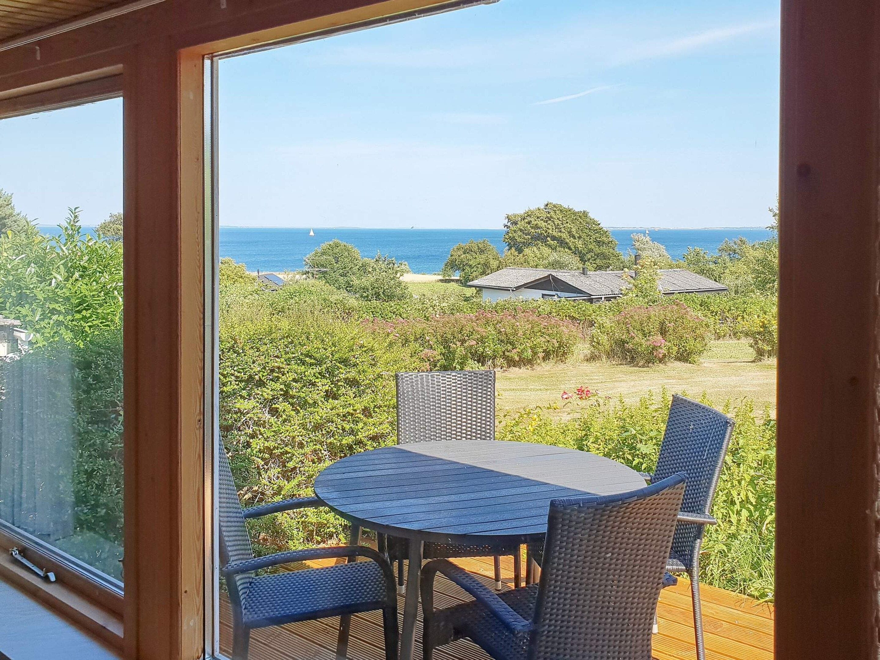 Un balcon avec une table et des chaises, donnant sur un jardin et la mer.