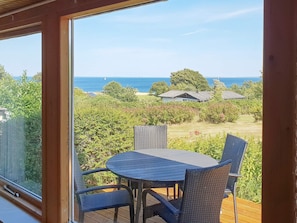 A balcony with a table and chairs, overlooking a garden and the sea. - Rustic Holiday Home in Augustenborg near Sea (Augustenborg)